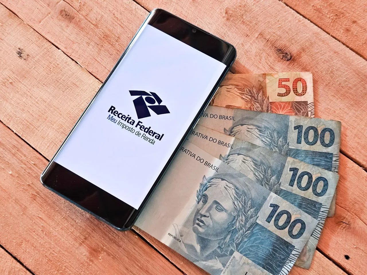 O que é a restituição do Imposto de Renda? | Foto de um celular sobre notas de dinheiro | Certificação Digital | Blog da Certisign