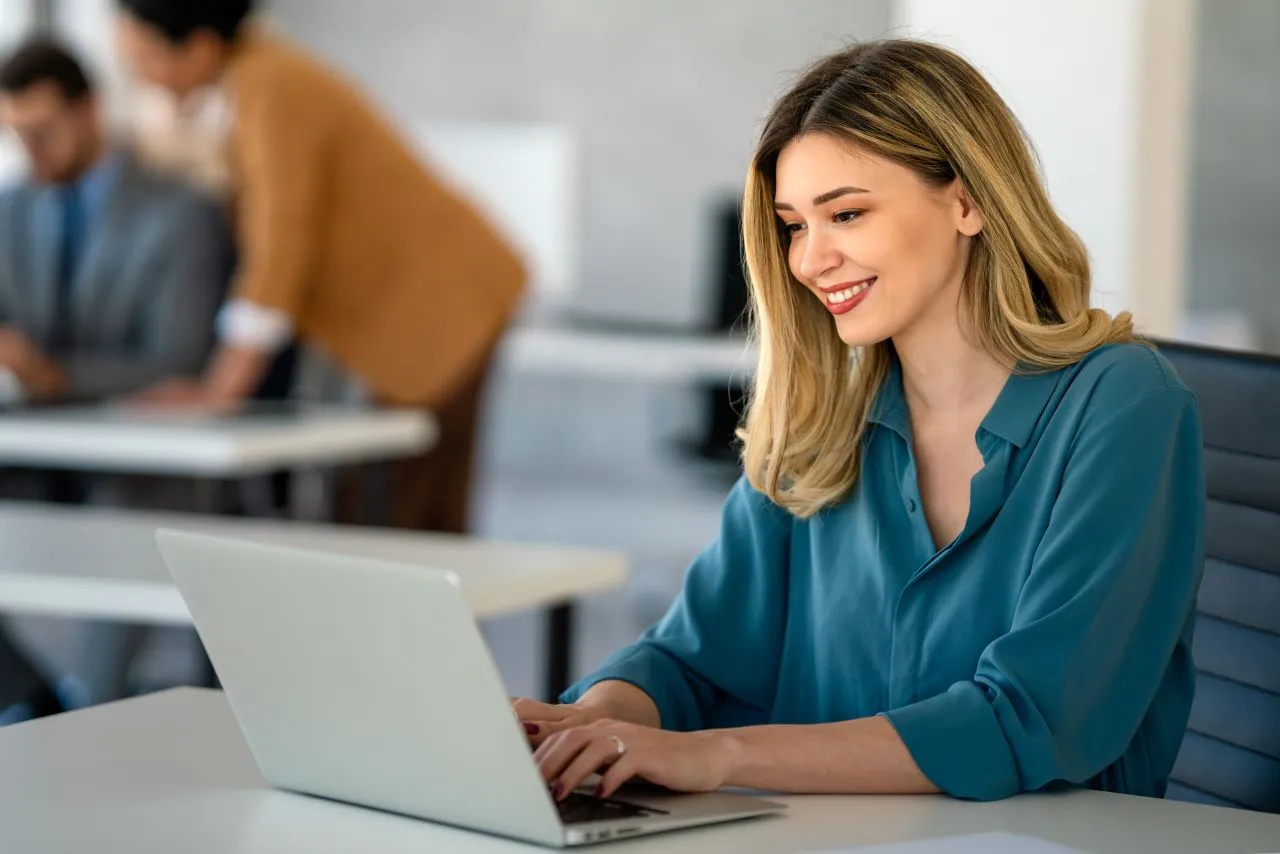O que é o PJe | Foto de uma mulher branca e loira sorrindo trabalhando no computador | Certificado Digital | Blog da CertiSign