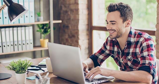 Foto de um homem sorrindo utilizando um notebook