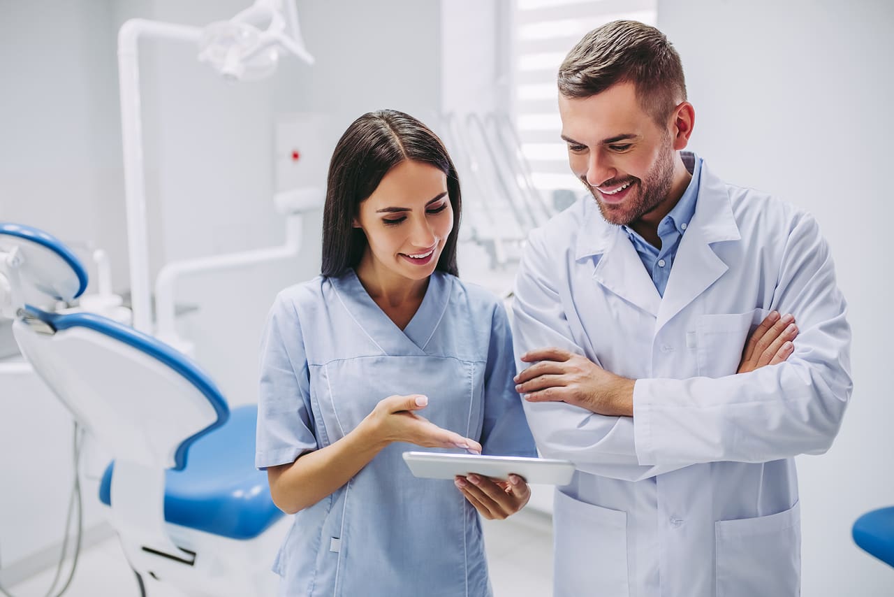 Vantagens da assinatura digital na clínica odontológica | Foto de uma dentista e de um dentista analisando prontuário eletrônico de paciente no tablet | Profissionais da Saúde | Blog da Certisign